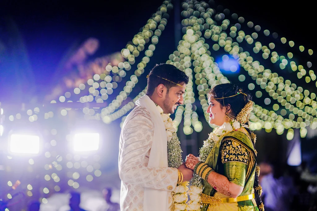 A couple sharing a moment beneath white flowers and evening lights
