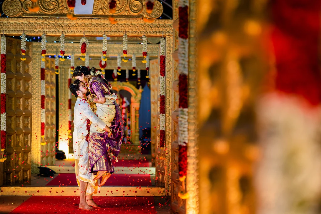 A groom lifting his bride under an ornate gold wedding canopy